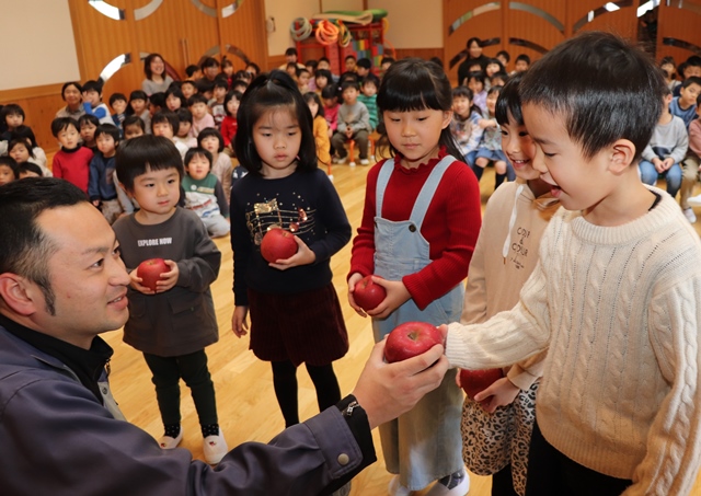 丸果七尾青果株式会社の川内さんからリンゴを受け取る園児たち