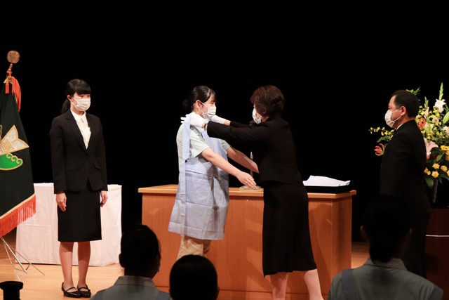 赤島学校長からエプロンをかけてもらう生徒