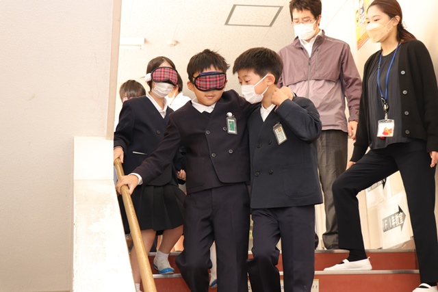 アイマスクを着けて階段を下る児童と補助する児童
