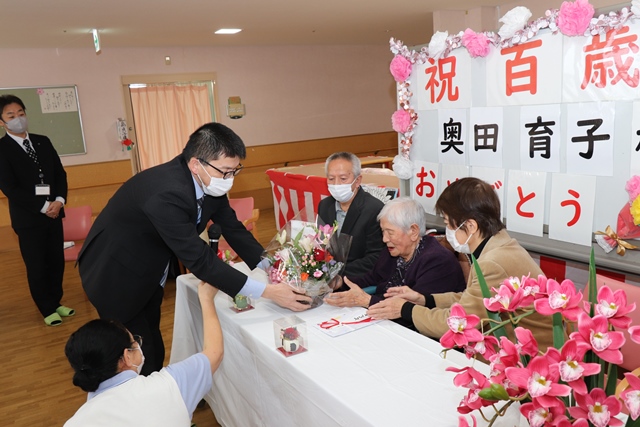 市からお祝いの花かごを受け取る育子さん