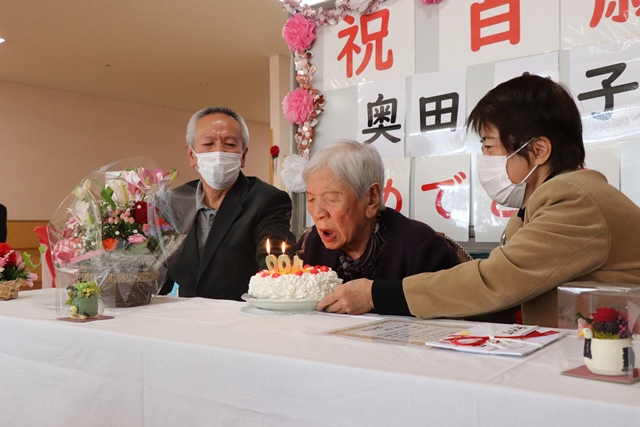 誕生日ケーキに立てられたロウソクの火を消す育子さん