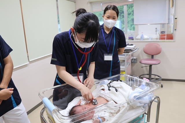 新生児に聴診器を当てる高校生
